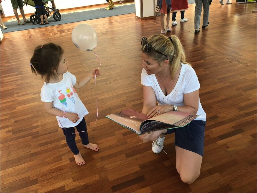 A mother kneeling on the floor to read a Fairy Dalia book to her child
